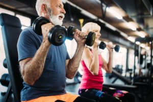 Duas pessoas na faixa dos 60 anos usando pesos em uma academia.